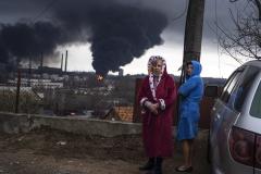 Women stand in their robes as smoke rises in the background after shelling in Odesa, Ukraine, Sunday, April 3, 2022. (AP Photo/Petros Giannakouris)