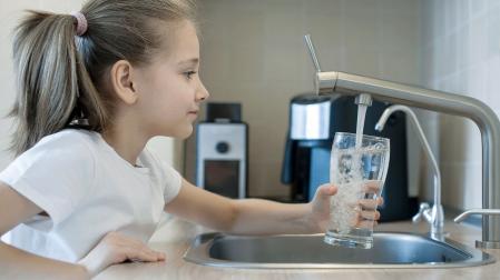 Una niña se sirve un vaso de agua del grifo